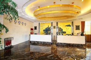 Un vestíbulo de hotel con una recepción, una lámpara de araña grande y un mural en la pared.