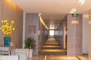Vestíbulo de hotel con mostrador de recepción, una planta y un cartel que indica la dirección al ascensor.