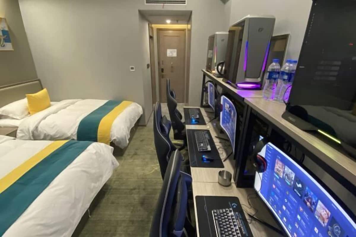 Quarto de hotel com duas camas, uma escrivaninha com computadores e um monitor grande.