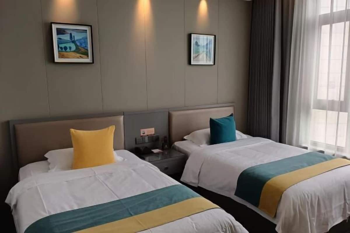 Quarto de hotel com duas camas, uma mesa de cabeceira e duas fotografias emolduradas na parede.