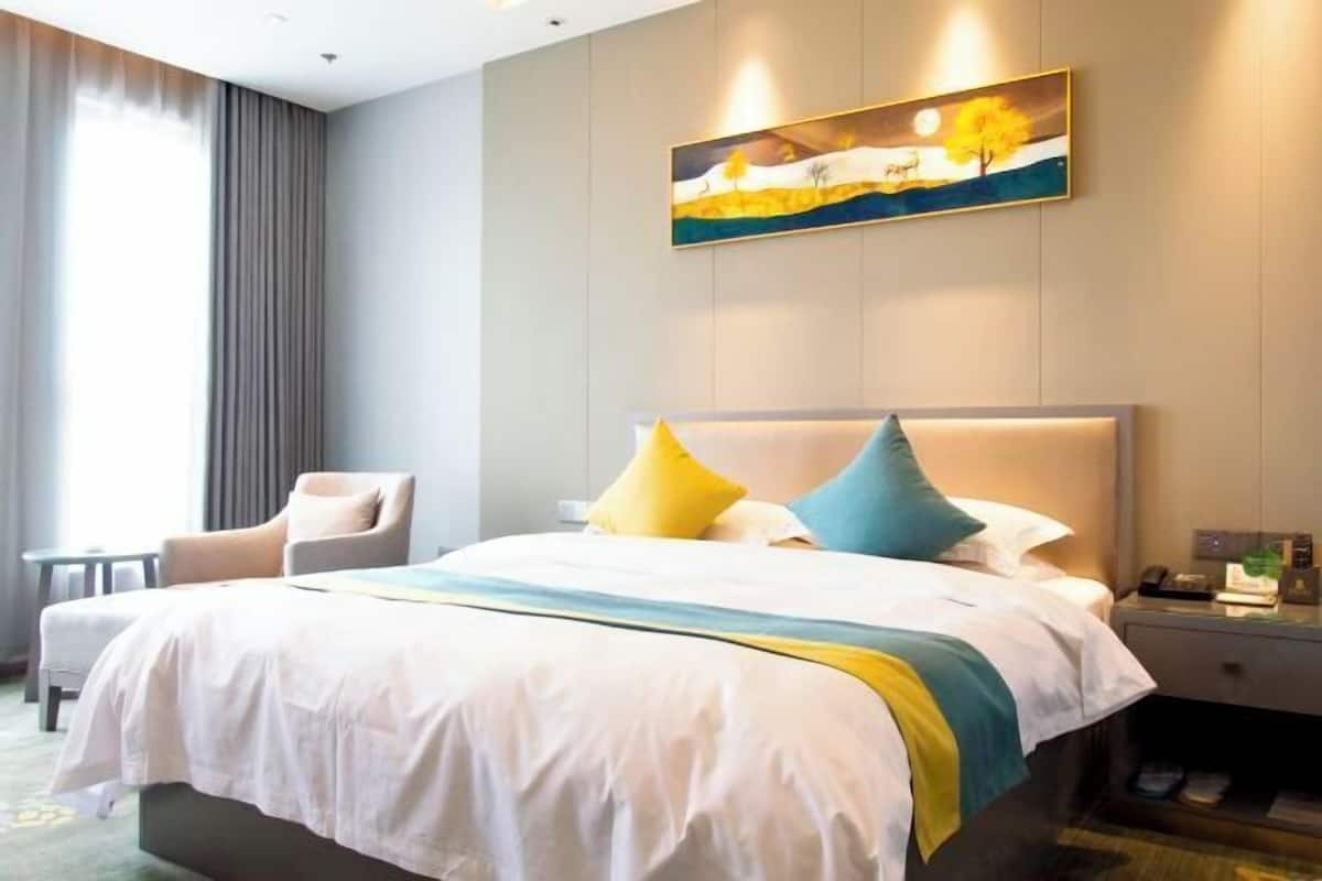Quarto de hotel com cama, uma cadeira, mesa de cabeceira e um quadro na parede.
