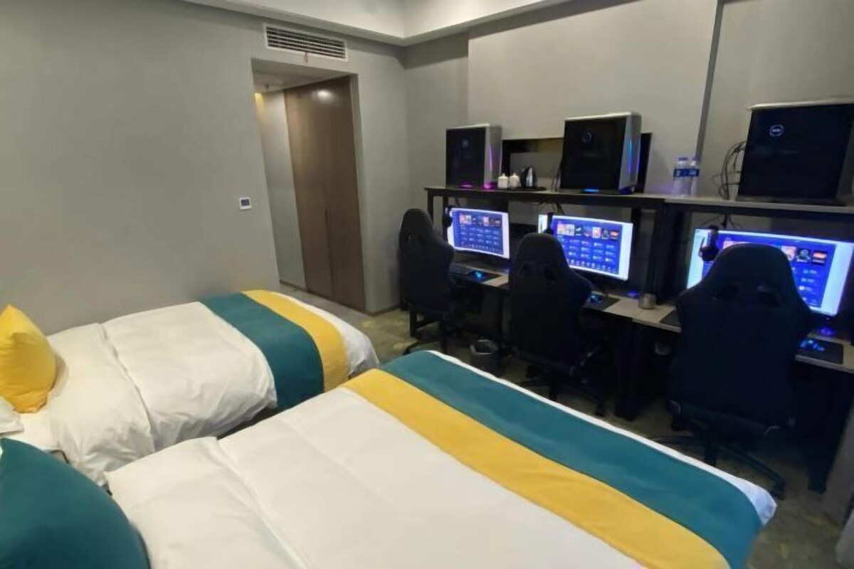 A hotel room with two beds, a desk with computers, and a door leading to another room.