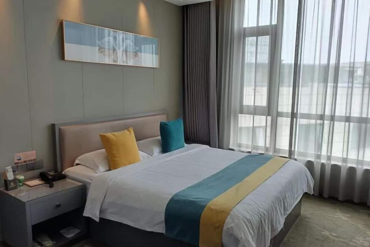 Quarto de hotel com cama, mesa de cabeceira, um quadro na parede e janela com cortinas.