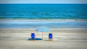A beach with two blue and white striped umbrellas and two blue chairs facing the ocean. - Private Hot Tub with outdoor shower and tiki area to relax and Enjoy! (Galveston)