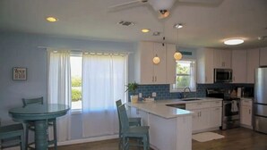 A modern kitchen with white cabinets, a central island, and a dining area with a glass table and chairs. - Private Hot Tub with outdoor shower and tiki area to relax and Enjoy! (Galveston)