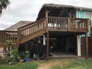 Une terrasse en bois surmontée d’un toit de chaume et dotée d’un escalier menant à un niveau supérieur.