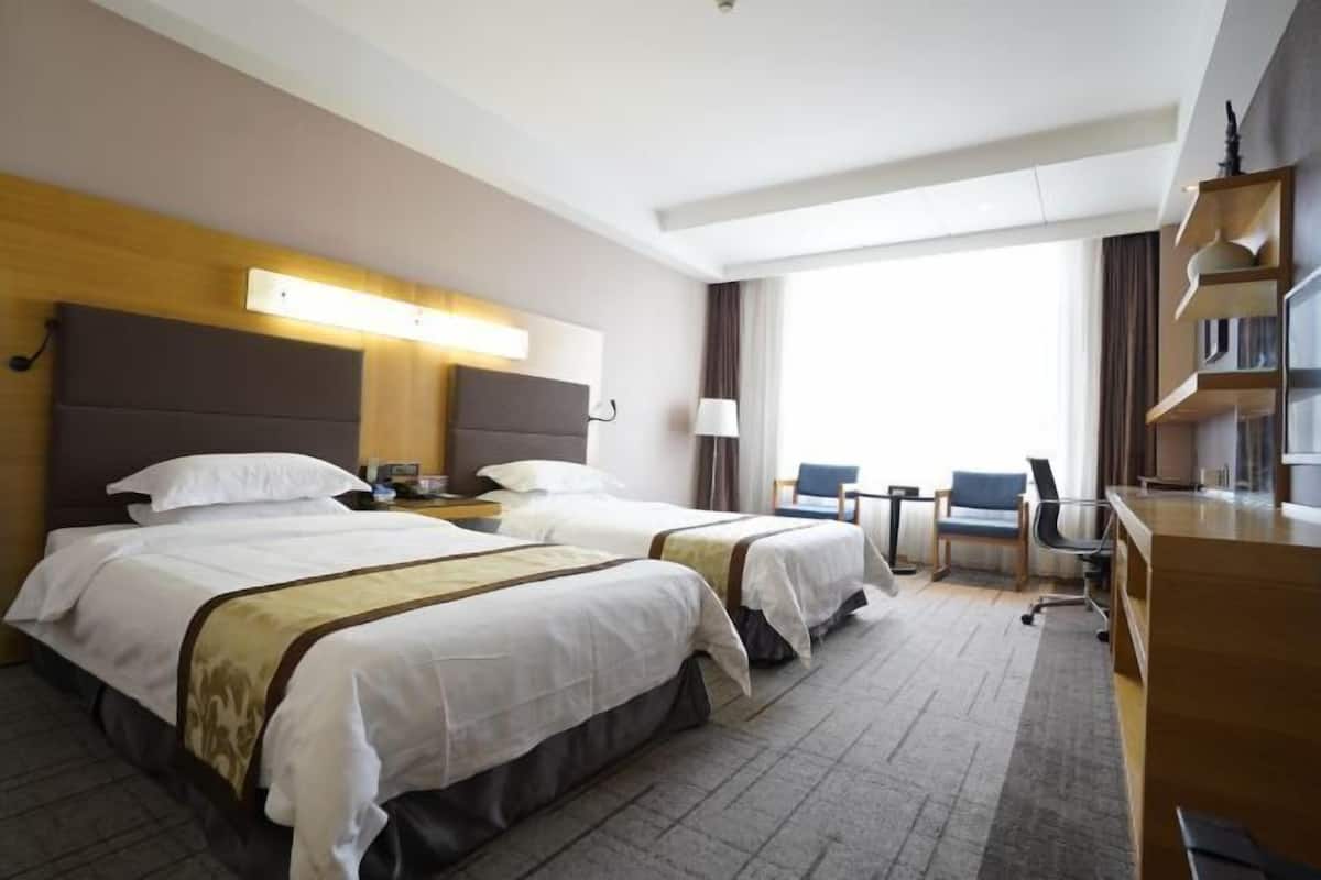 A hotel room with two beds, a desk, a chair, and a large window.