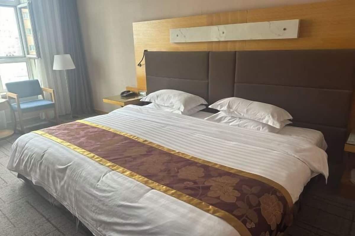 A hotel room with a large bed, a wooden headboard, a desk with a lamp, and a chair.