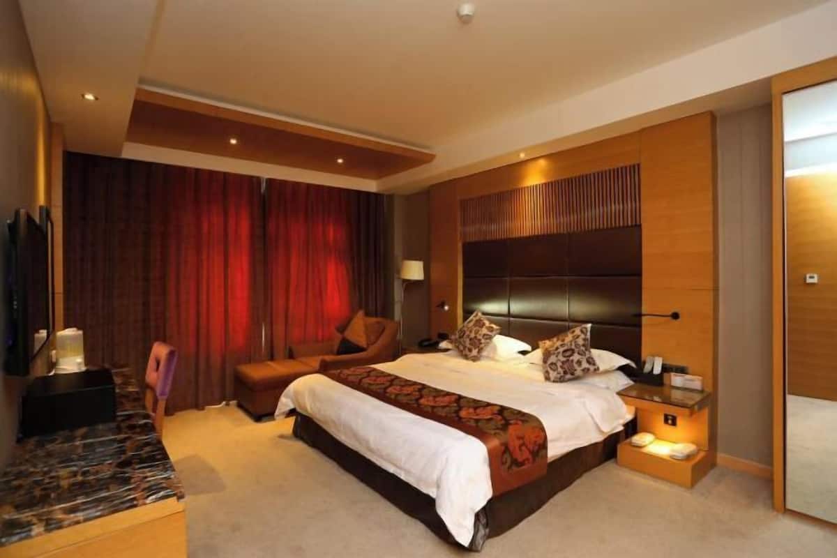 A hotel room with a large bed, a desk, a chair, a TV, and a wardrobe.
