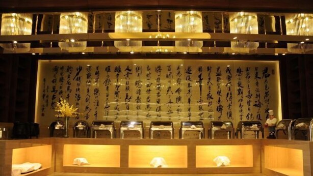 A reception area with a wall of calligraphy, a chandelier, and a row of chairs. - Hui Nan Hotel (Huinan)