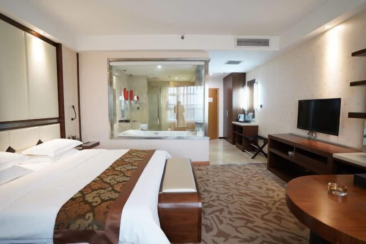 Une chambre d’hôtel équipée d’un lit, d’une télévision, d’un bureau et d’une salle de bain fermée par des parois de verre.