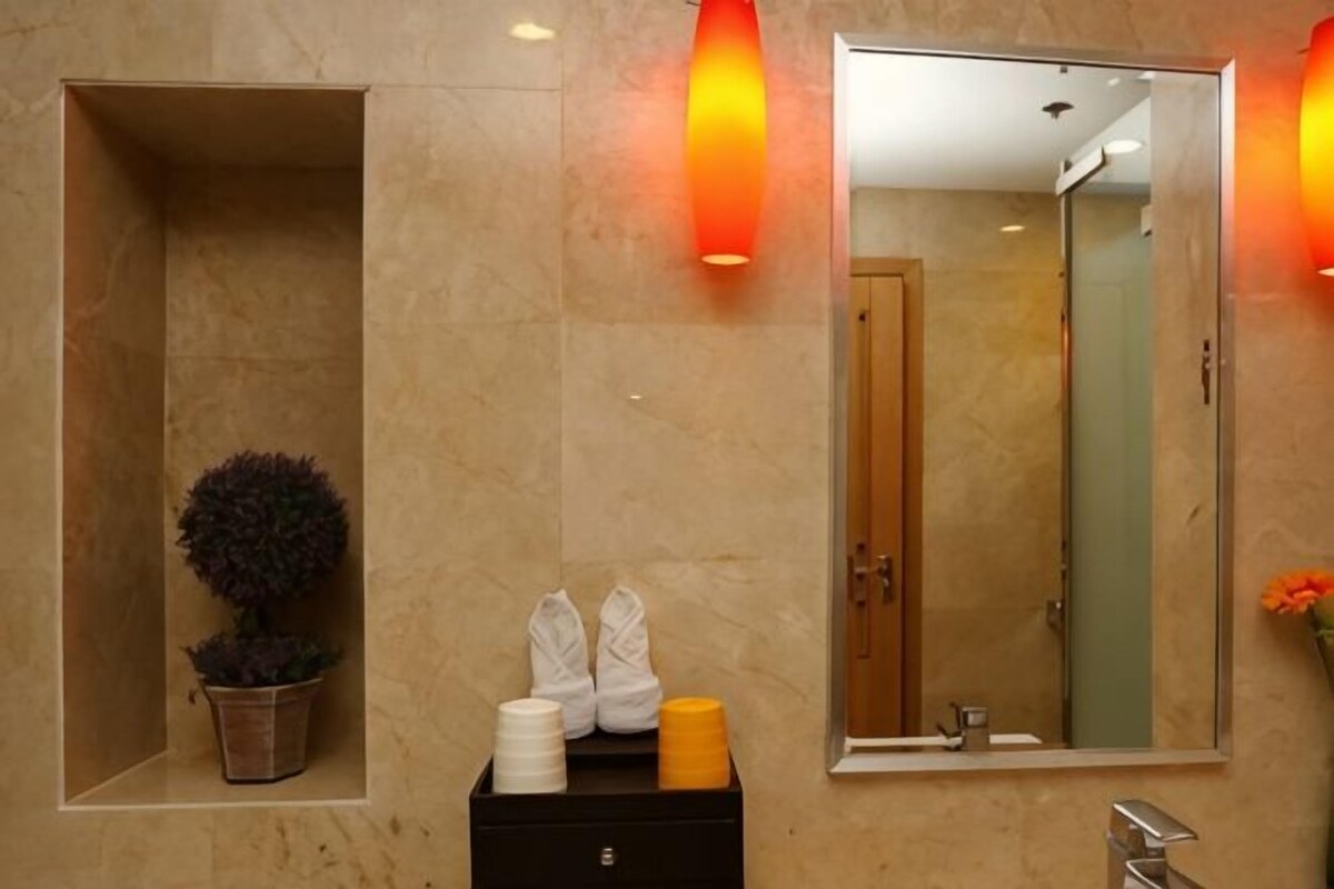 A bathroom with a large mirror, a potted plant, a black storage unit, and a wall-mounted light fixture.