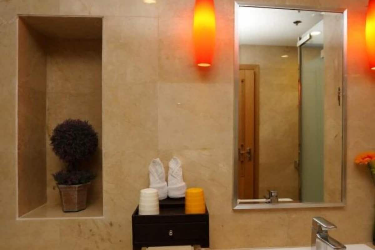 A bathroom with a marble wall, a mirror, a sink, a towel dispenser, and a potted plant.