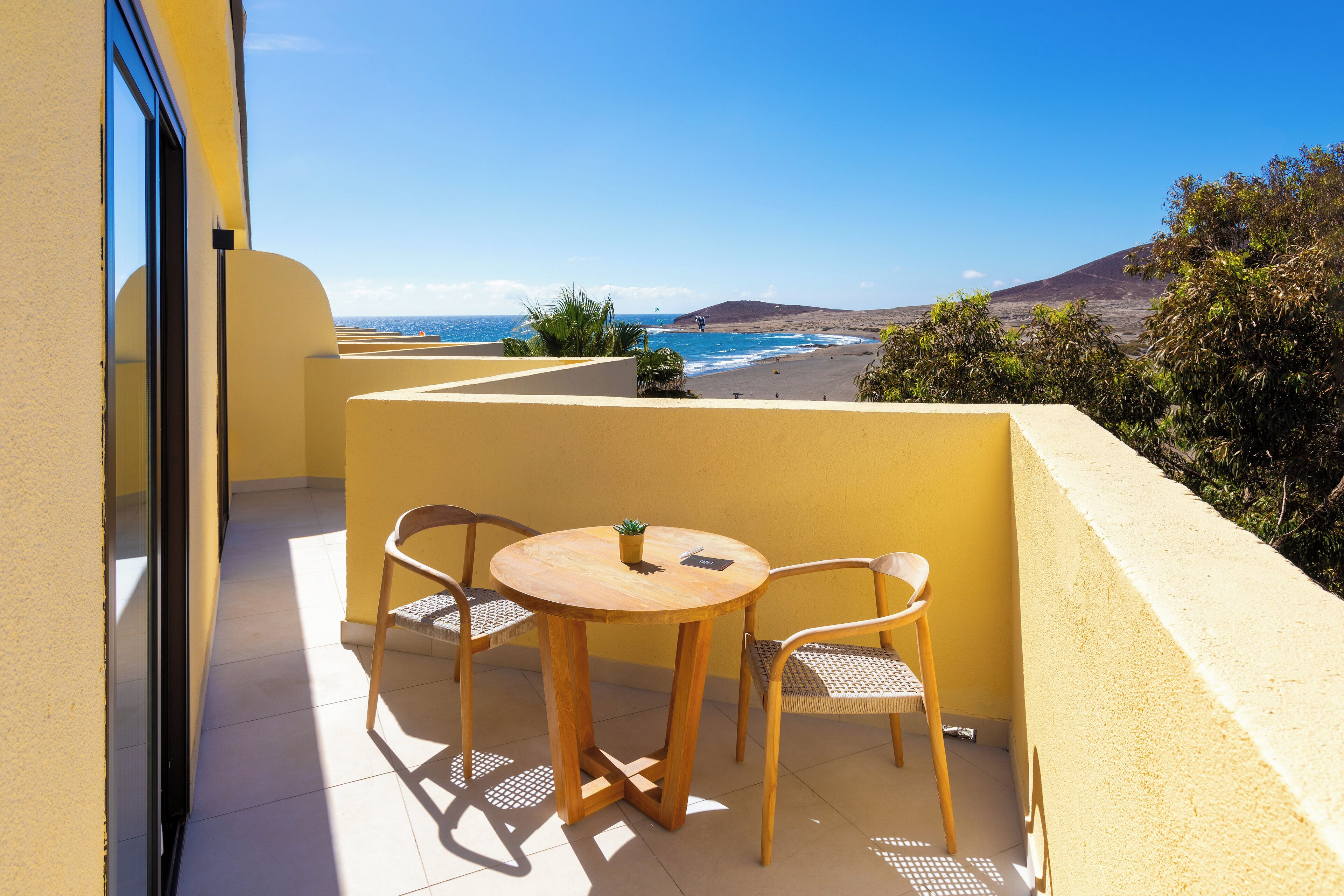 Un balcon avec une table et des chaises, donnant sur une plage et une montagne.