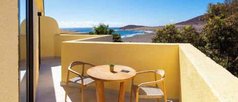 Un balcon avec une table et des chaises, donnant sur une plage et une montagne.