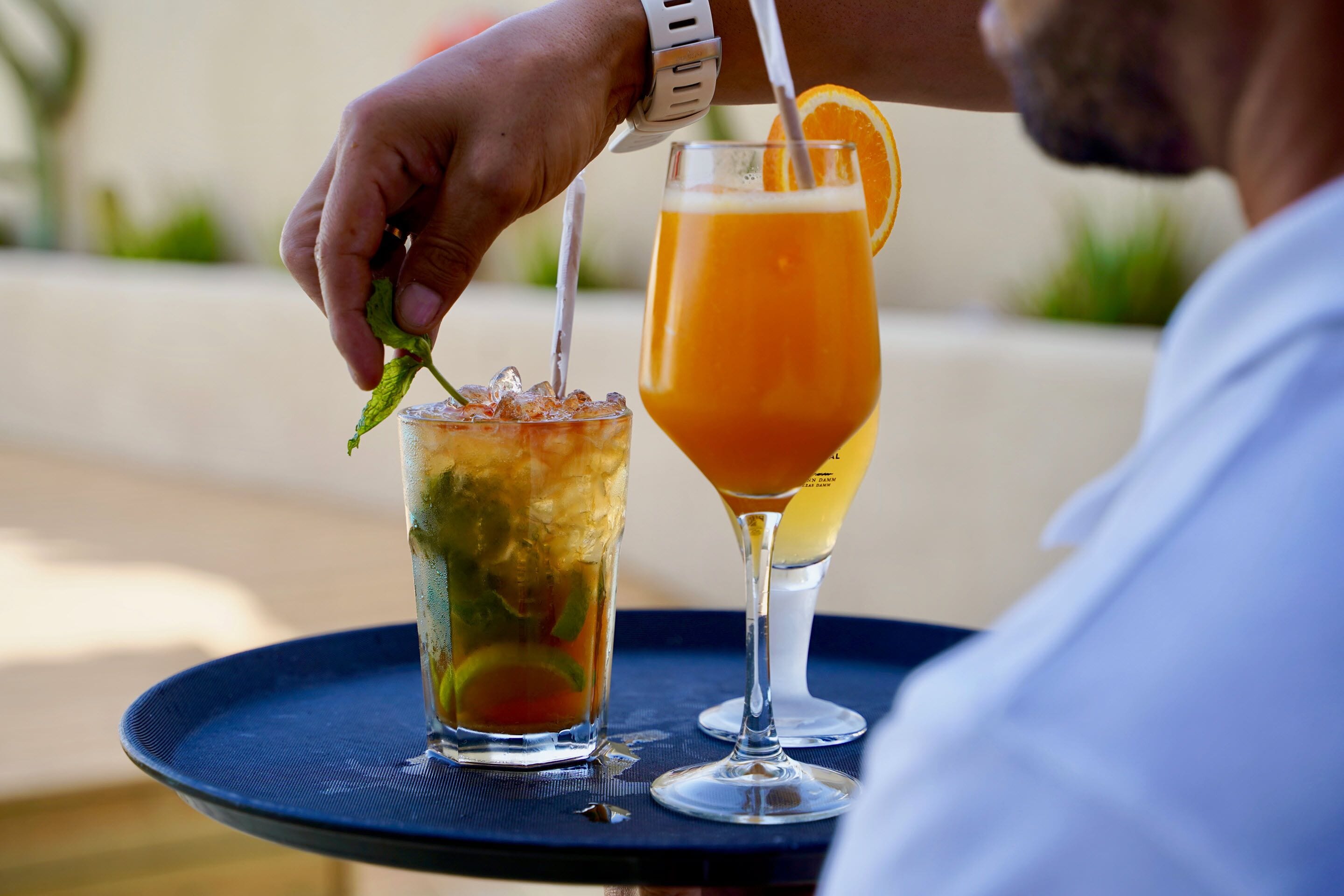 Dos bebidas en una bandeja, una con un adorno de lima y la otra con una rodaja de naranja.