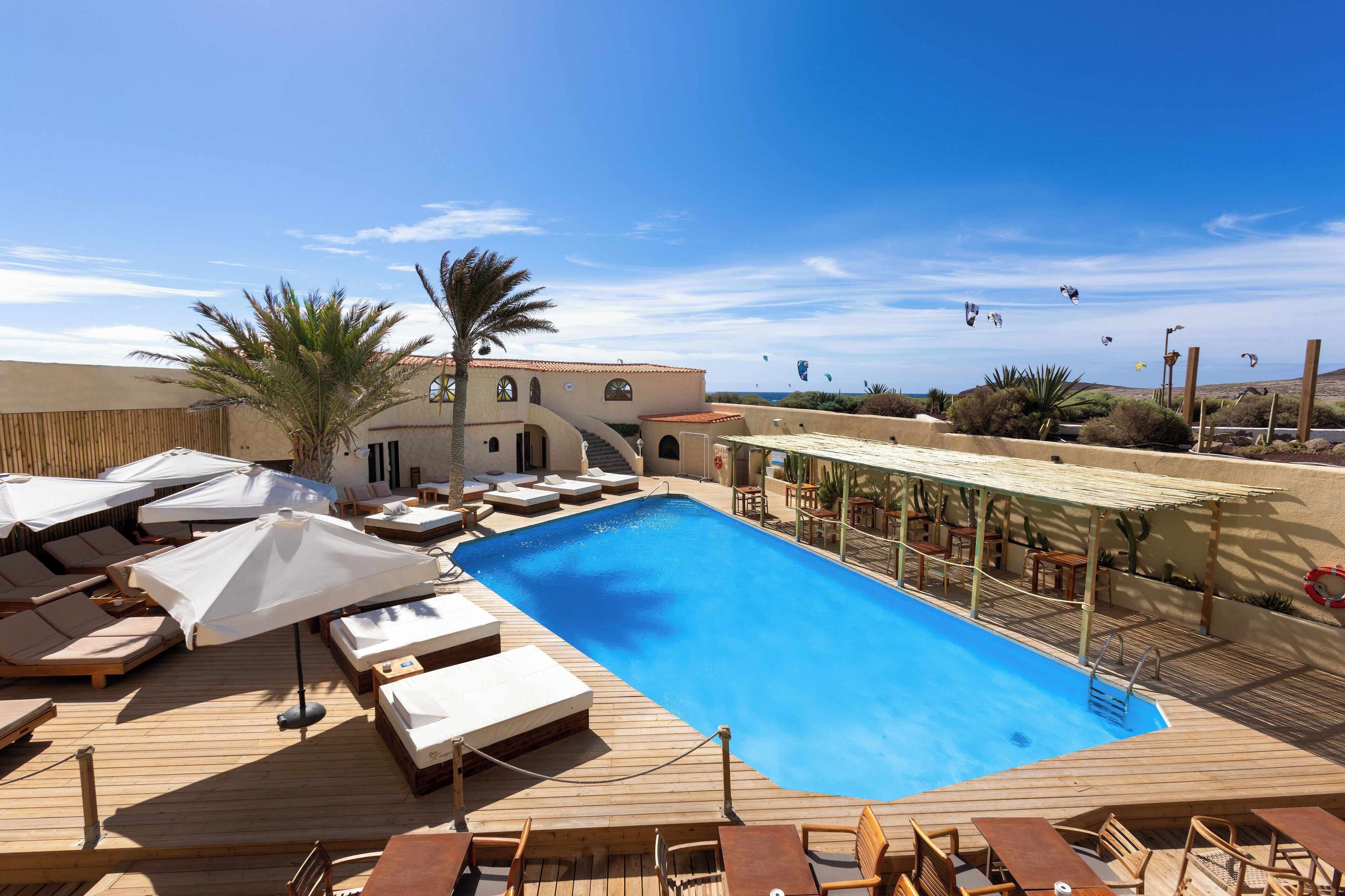 Un espace piscine avec des chaises longues, des parasols et une terrasse en bois.