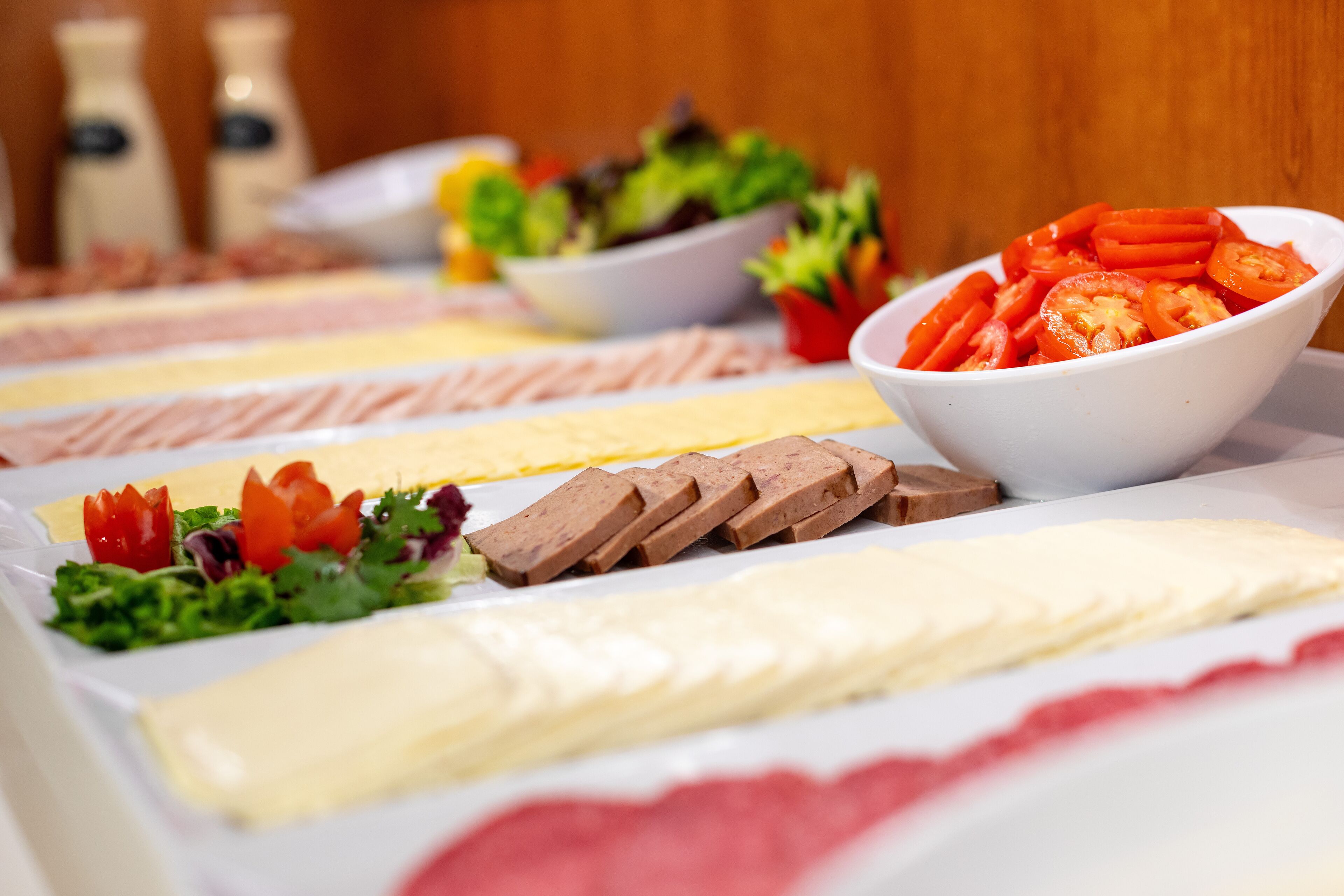 Une table de buffet proposant divers plats, notamment des tomates en tranches, une salade et un dessert.