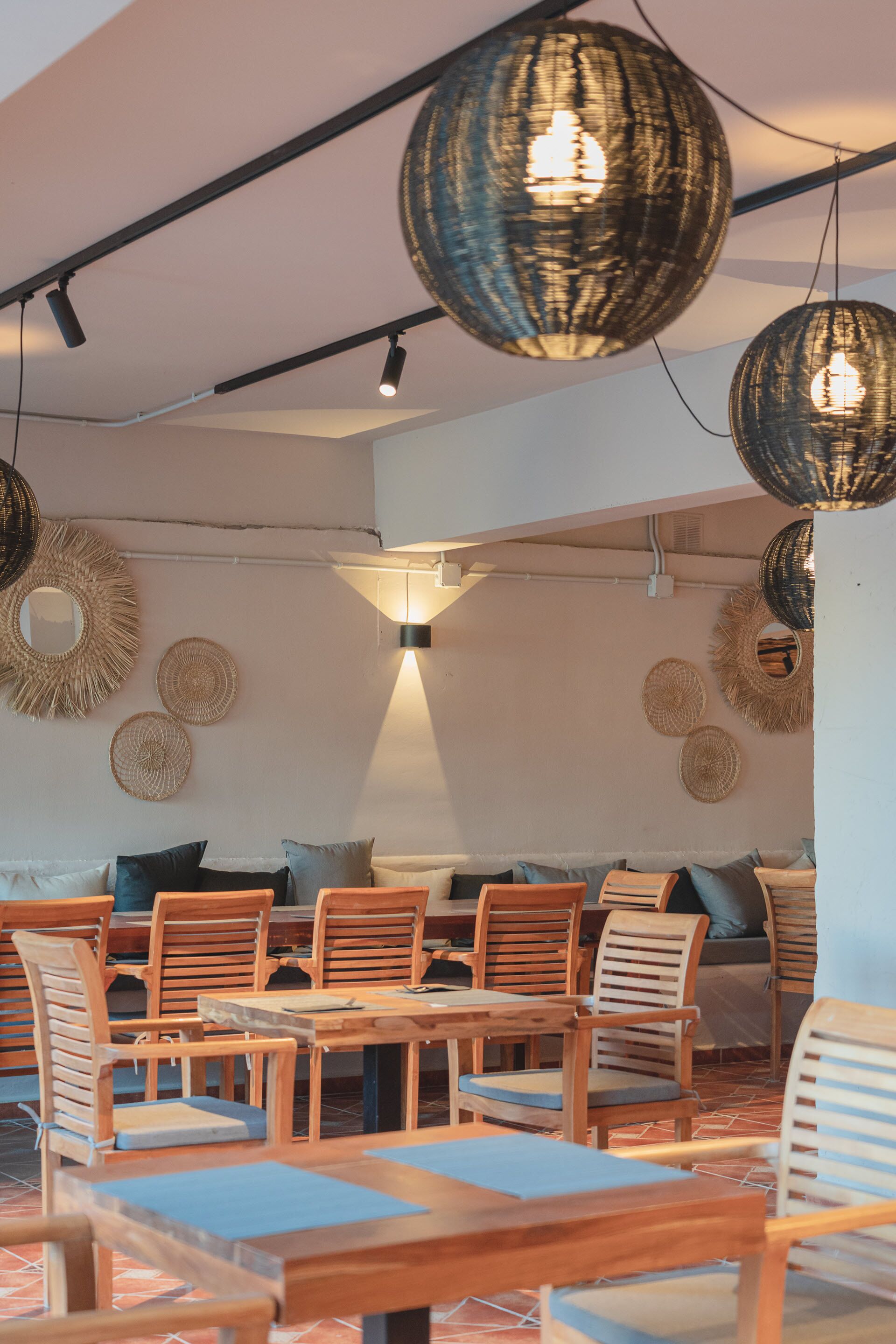A dining area with wooden tables and chairs, woven pendant lights, and wall-mounted woven decorations.