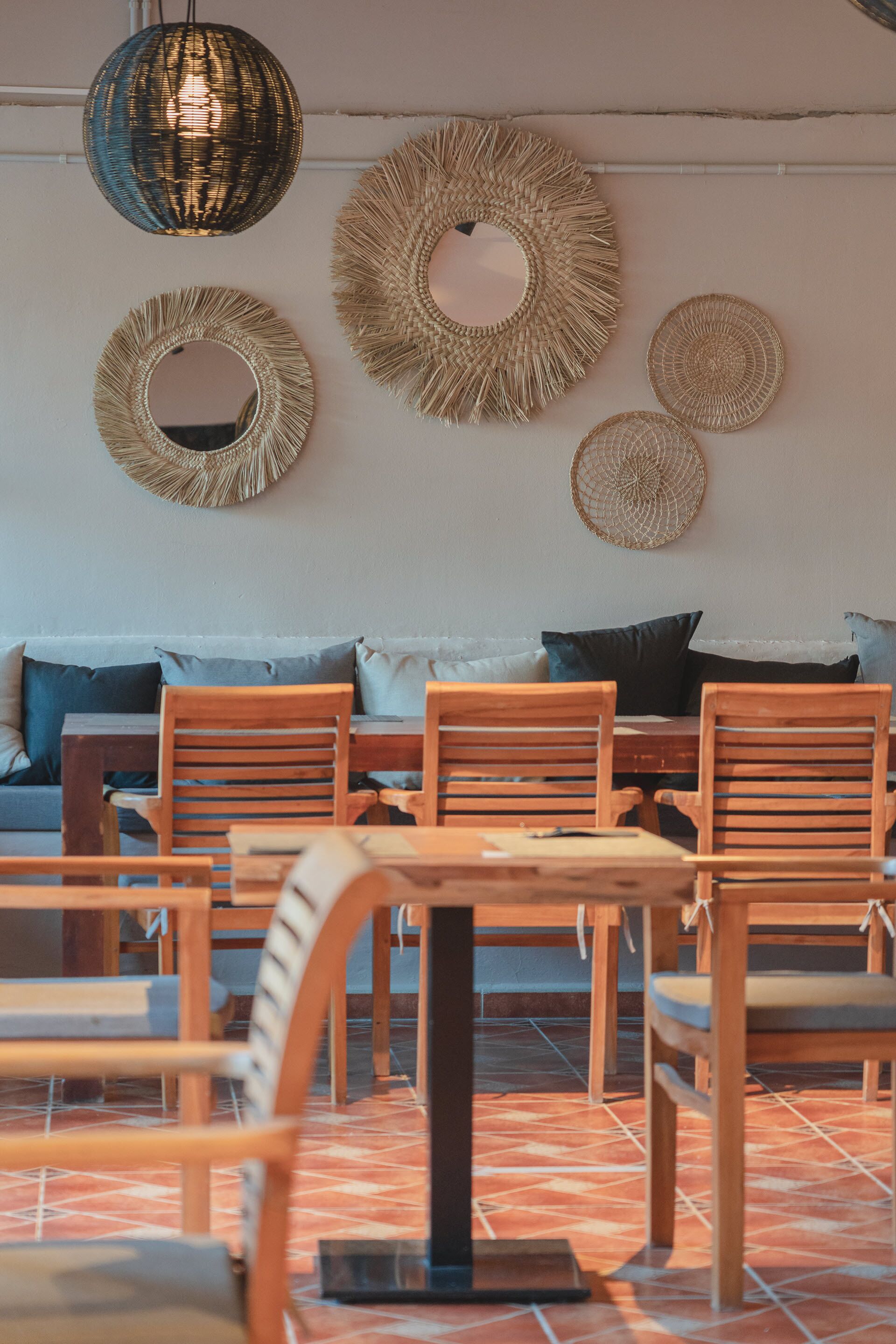 A dining area with wooden chairs and a table, surrounded by woven wall decorations and a hanging light fixture.
