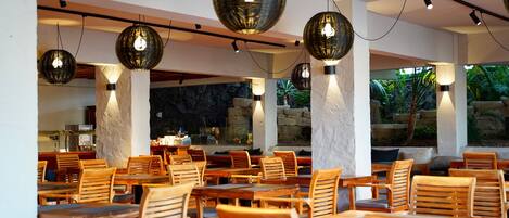 Un espace de restauration intérieur avec des tables et des chaises en bois, de grandes lampes sphériques décoratives et une vue sur un cadre naturel grâce à de grandes fenêtres.