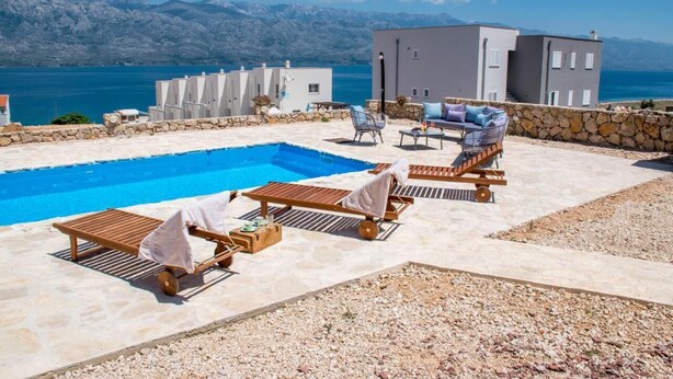 A pool area with lounge chairs, a stone wall, and a view of the sea and mountains. - Wild Wind Residence (Razanac)