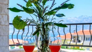A round metal table with two glasses of red drink, a potted plant, and a view of a building and mountains in the background. - Wild Wind Residence (Razanac)