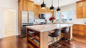 A modern kitchen with wooden cabinets, a large island, bar stools, and pendant lighting.