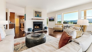 A spacious living room with a fireplace, a sofa, a coffee table, and a view of the outdoors through large windows.