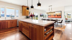 A modern kitchen with wooden cabinets, a large island, pendant lighting, and a view of the outdoors.