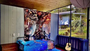Een slaapkamer met een bed, een gitaar en een groot raam met uitzicht op groen.