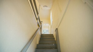 A narrow stairway with a handrail, leading to a landing with a door and a poster.