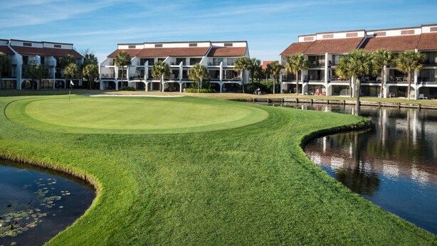 Un campo de golf bien cuidado con un estanque, rodeado de edificios de varios pisos con balcones.