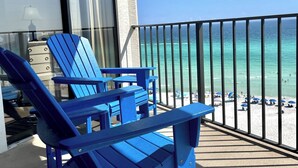 Un balcón con sillas Adirondack azules, vista al océano y una playa con sombrillas.