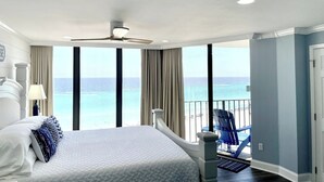 Una habitación de hotel con una cama grande, un ventilador de techo y vista al océano.