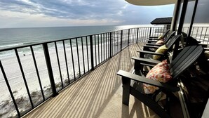 Ein Balkon mit Blick auf Strand und Meer. Mehrere Liegestühle und ein Tisch mit Kissen sind vorhanden.