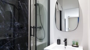 Ein modernes Badezimmer mit einer gläsernen Duschkabine, einem weißen Waschbecken mit Spiegel darüber und Toilettenartikeln auf dem Waschbecken.