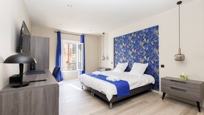 Ein modernes Hotelzimmer mit Bett, Nachttisch, Schreibtisch und einem großen Fenster mit Vorhängen.