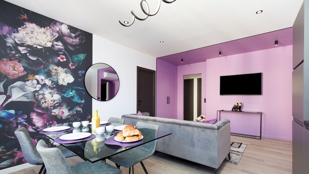 Ein modernes Wohnzimmer mit Essbereich, ausgestattet mit einer Couch, einem Glastisch und einem farbenfrohen Blumenwandbild.