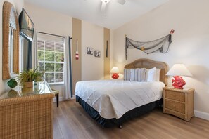 Een slaapkamer met een bed, nachtkastjes, een raam, een aan de muur bevestigde televisie en een plafondventilator.