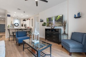 Un salon moderne avec une table basse en verre, un canapé bleu et un coin repas comprenant des chaises et une table.
