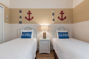 A room with two beds, each with a pillow labeled 'ALOHA,' a small bedside table with a lamp, and wall decorations including anchors and the words 'BEACH' and 'RELAX.' - Newly renovated beautiful second floor condo in Bahama Bay (Davenport)