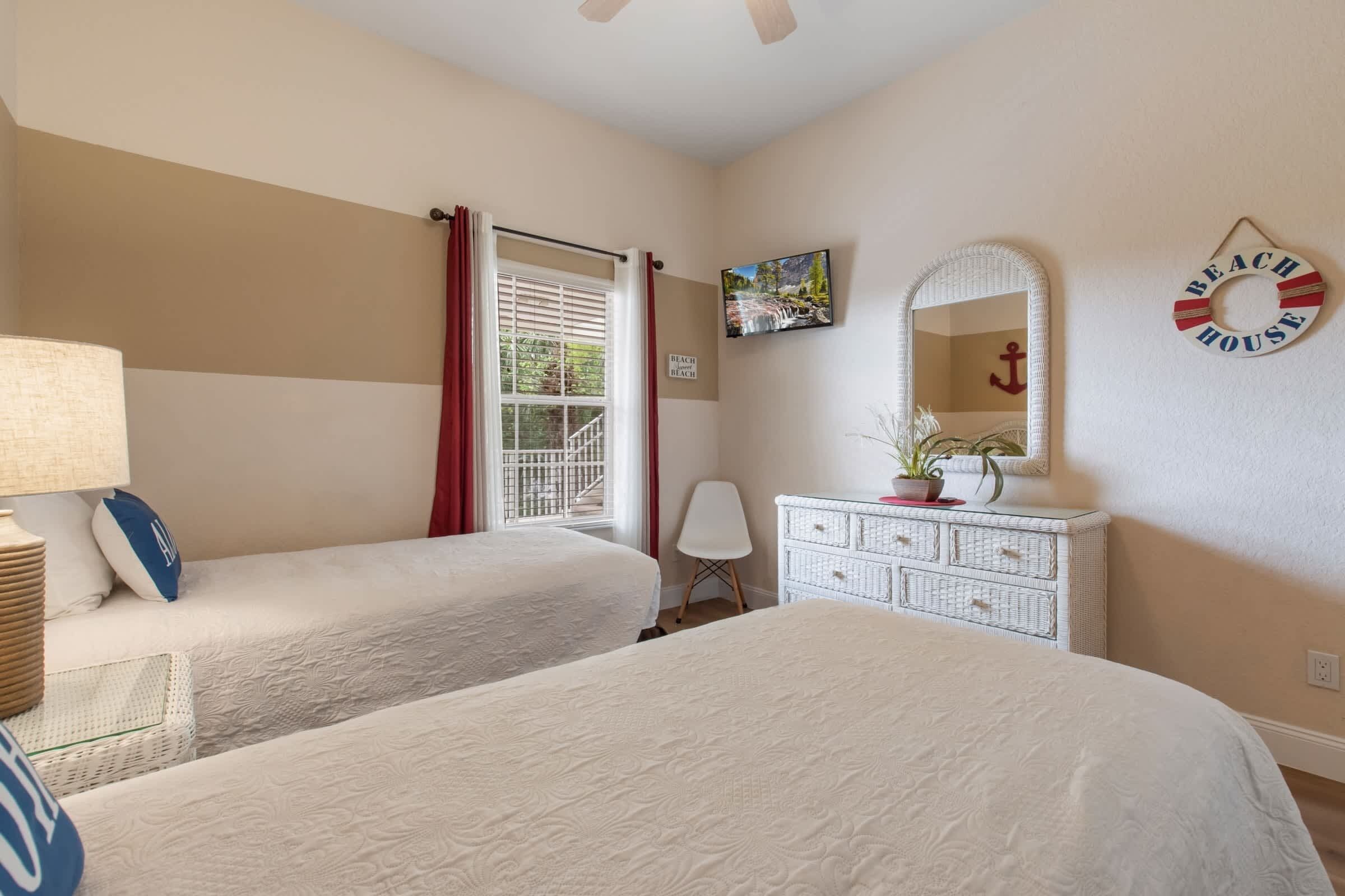 Une chambre avec deux lits, une commode, un miroir, une fenêtre avec des rideaux et un élément décoratif mural.