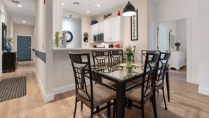 A modern kitchen with white cabinets, a microwave, and a dining area with a glass table and chairs.