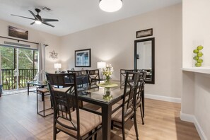 A dining area with a glass table, dark chairs, a ceiling fan, a framed picture, and a window with a view of greenery. - Newly renovated beautiful second floor condo in Bahama Bay (Davenport)