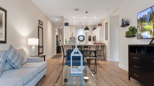 A modern living room with a glass coffee table, a sofa, a dining area with chairs, and a kitchen in the background.