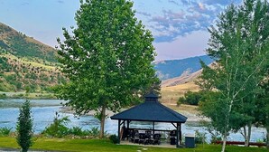 A gazebo with a roof and seating area by a lake, surrounded by trees and hills in the background. - Steelhead Lodge (Lucile)