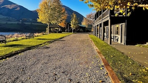A gravel path leading to a building with a covered outdoor area, benches, and a view of a lake and mountains. - Steelhead Lodge (Lucile)