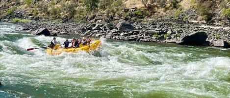 Een groep mensen in een gele raft die over een rivier vaart, omringd door rotsachtig terrein en schaarse begroeiing.