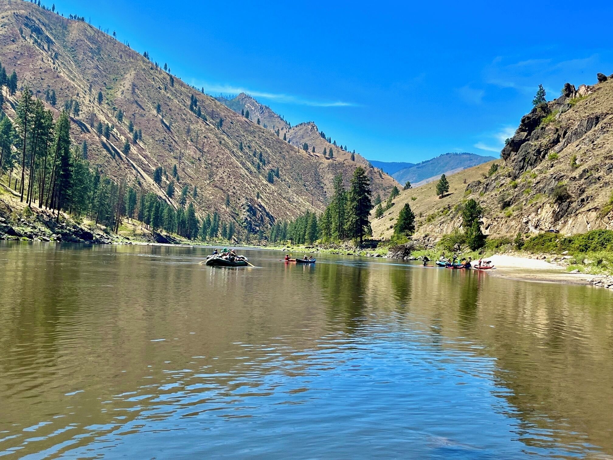 A river with boats, surrounded by mountains and trees.